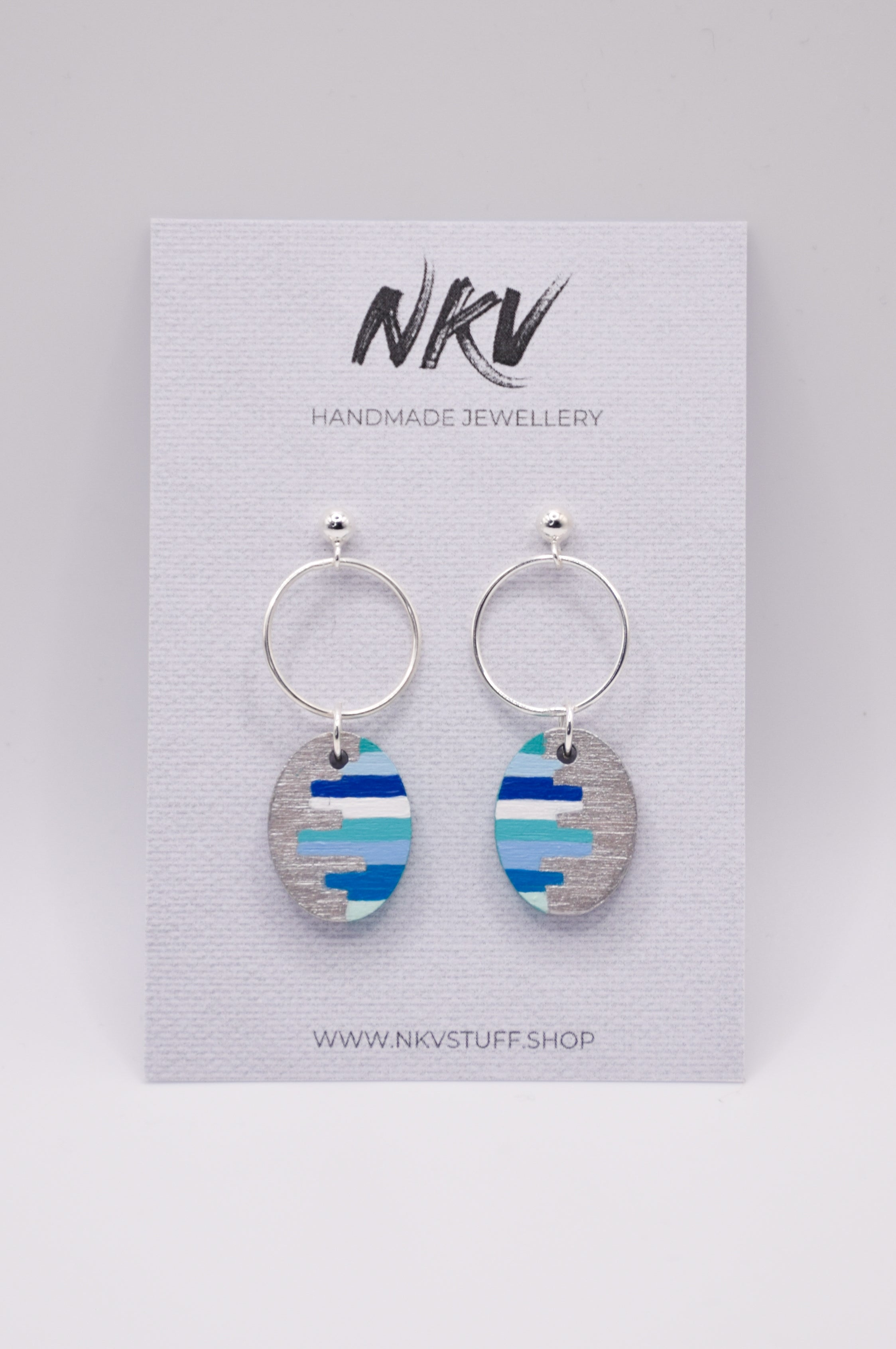 Pair of hand-painted earrings with blue stripes on a card with 'NKV Handmade Jewellery' branding.