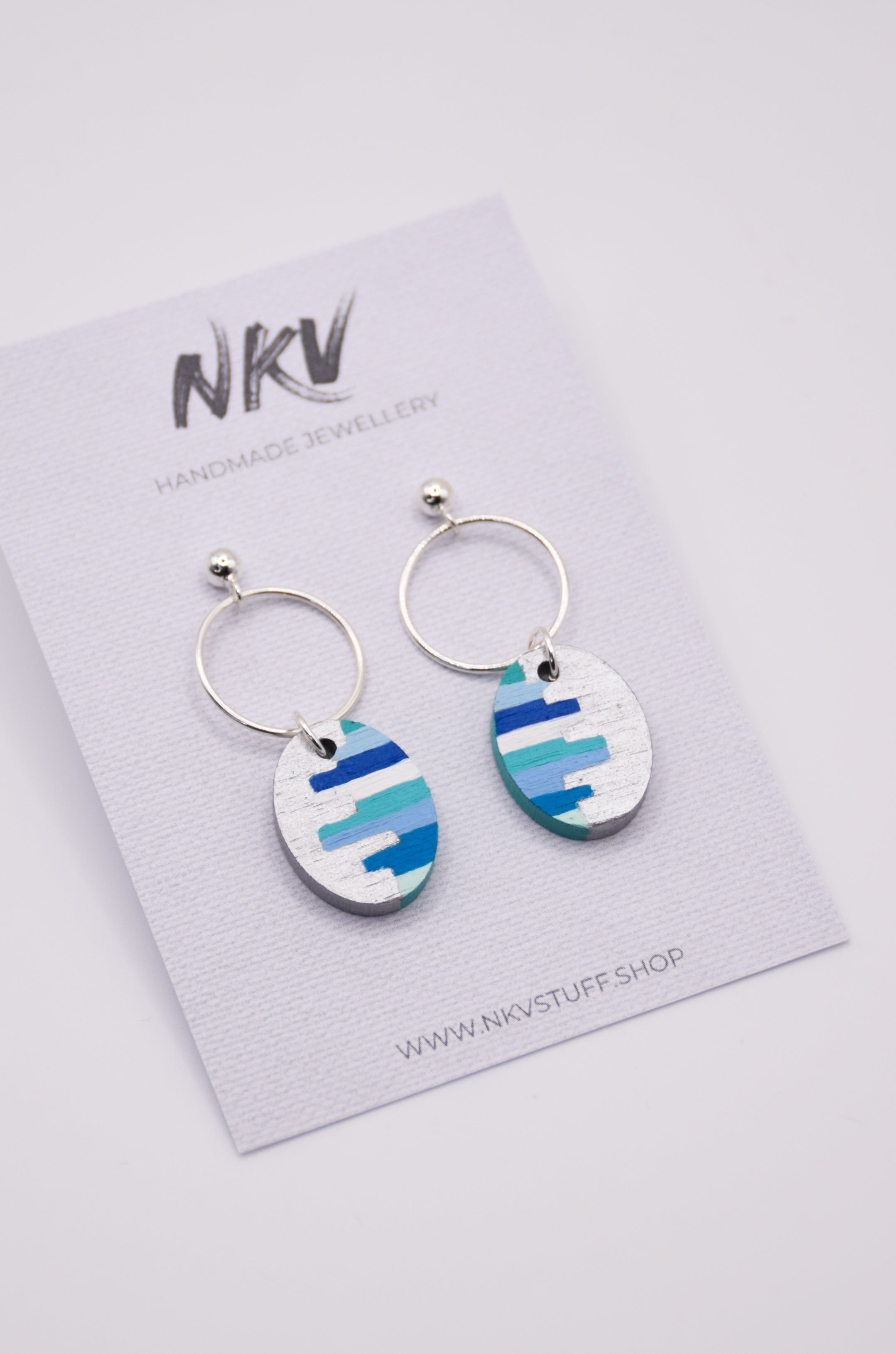 Pair of earrings with blue and green striped design on a NKV branded card.