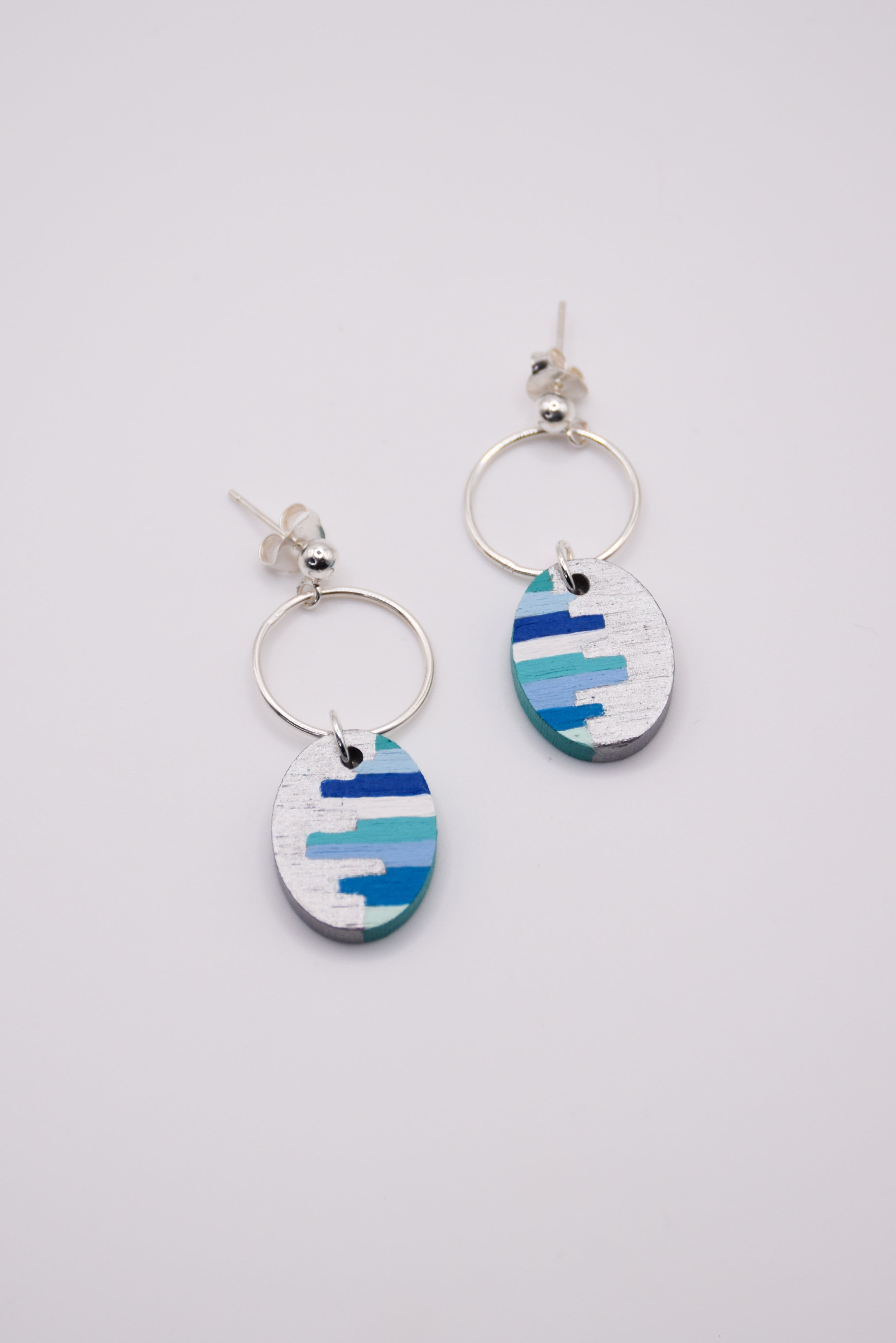 Pair of hand-painted earrings with blue and white striped design on a light gray background