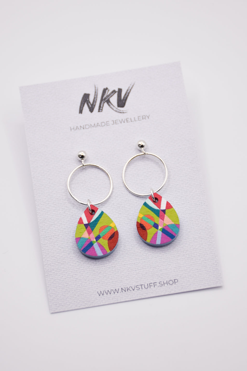 Colorful hand-painted teardrop earrings with silver hoops on a NKV branded card.