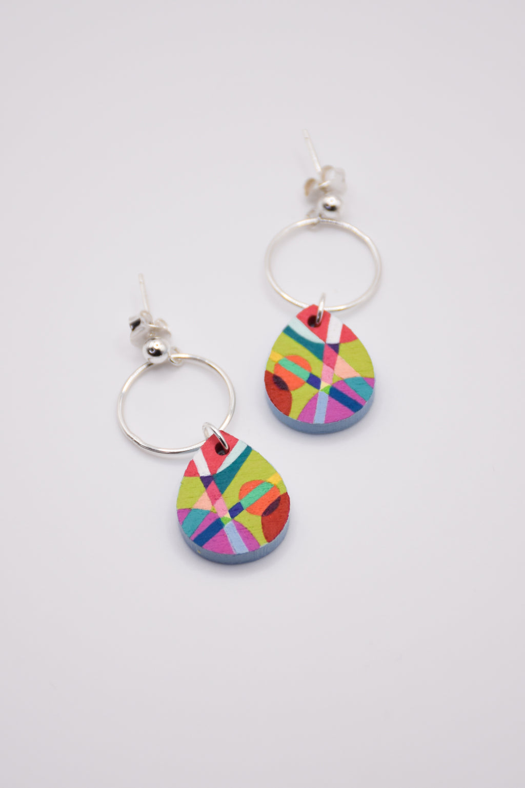 Colorful teardrop-shaped hand-painted earrings with silver hoops on a white background