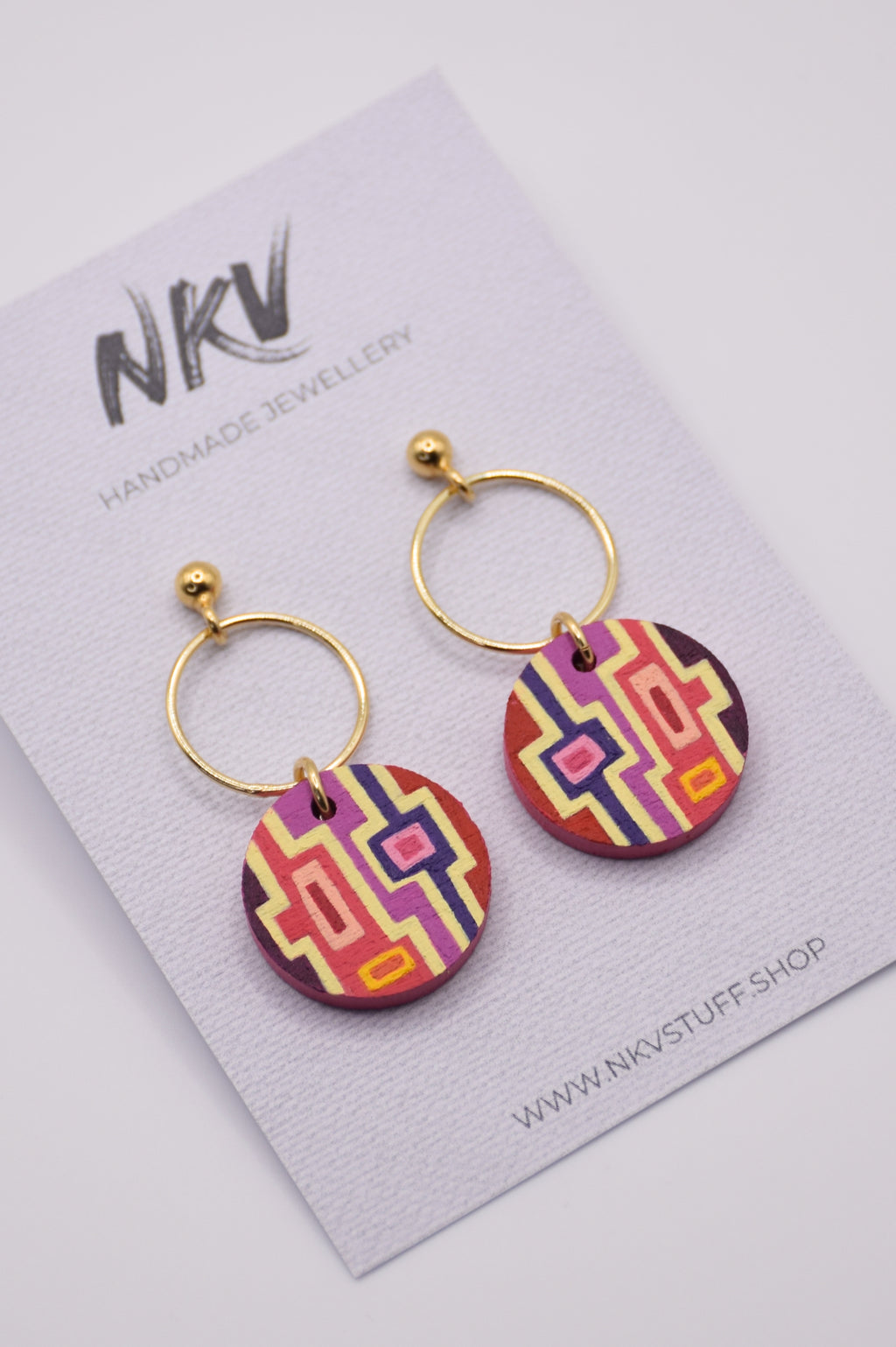 Colorful hand-painted geometric earrings with gold hoops on a NKV branded card